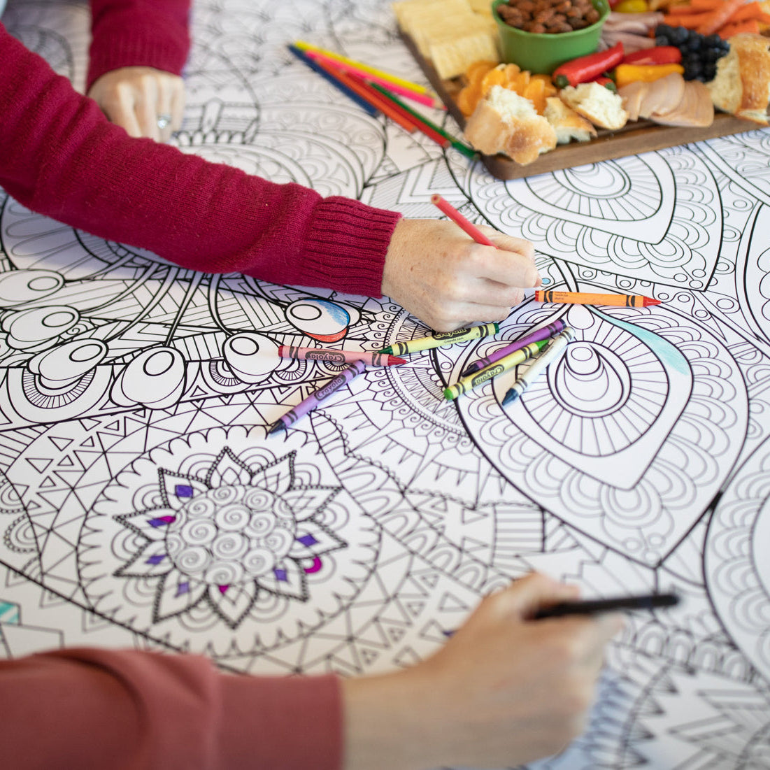 hands holding colored pencils coloring on a large coloring poster with a charcuterie board in the background