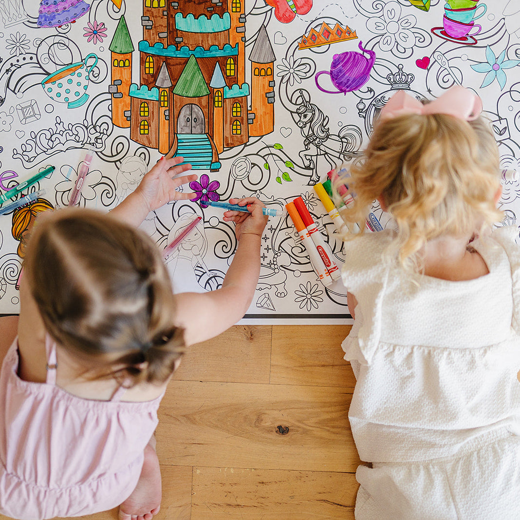 Two children coloring on a large sheet of paper with various drawings and text.