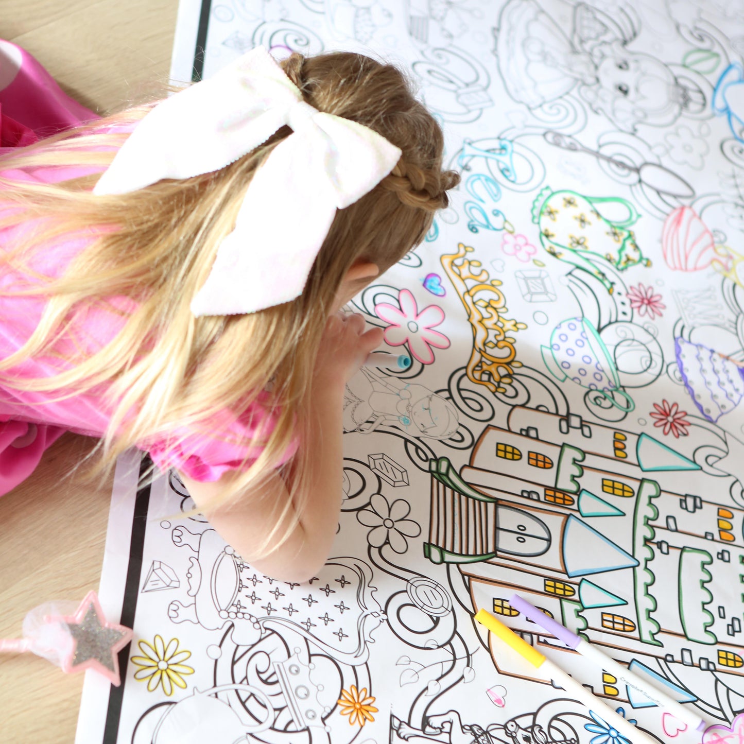 Child coloring a detailed picture of a princess castle with a large white bow on their head.