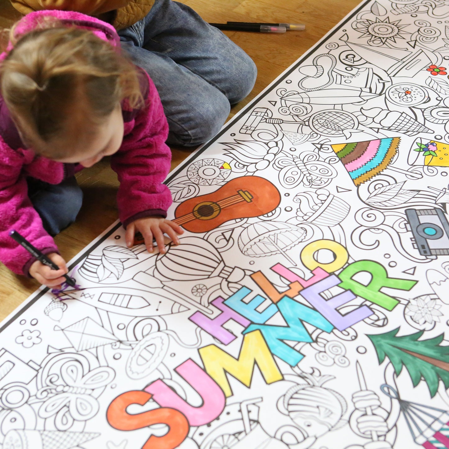 Child coloring a large 'Summer' themed coloring sheet on the floor.