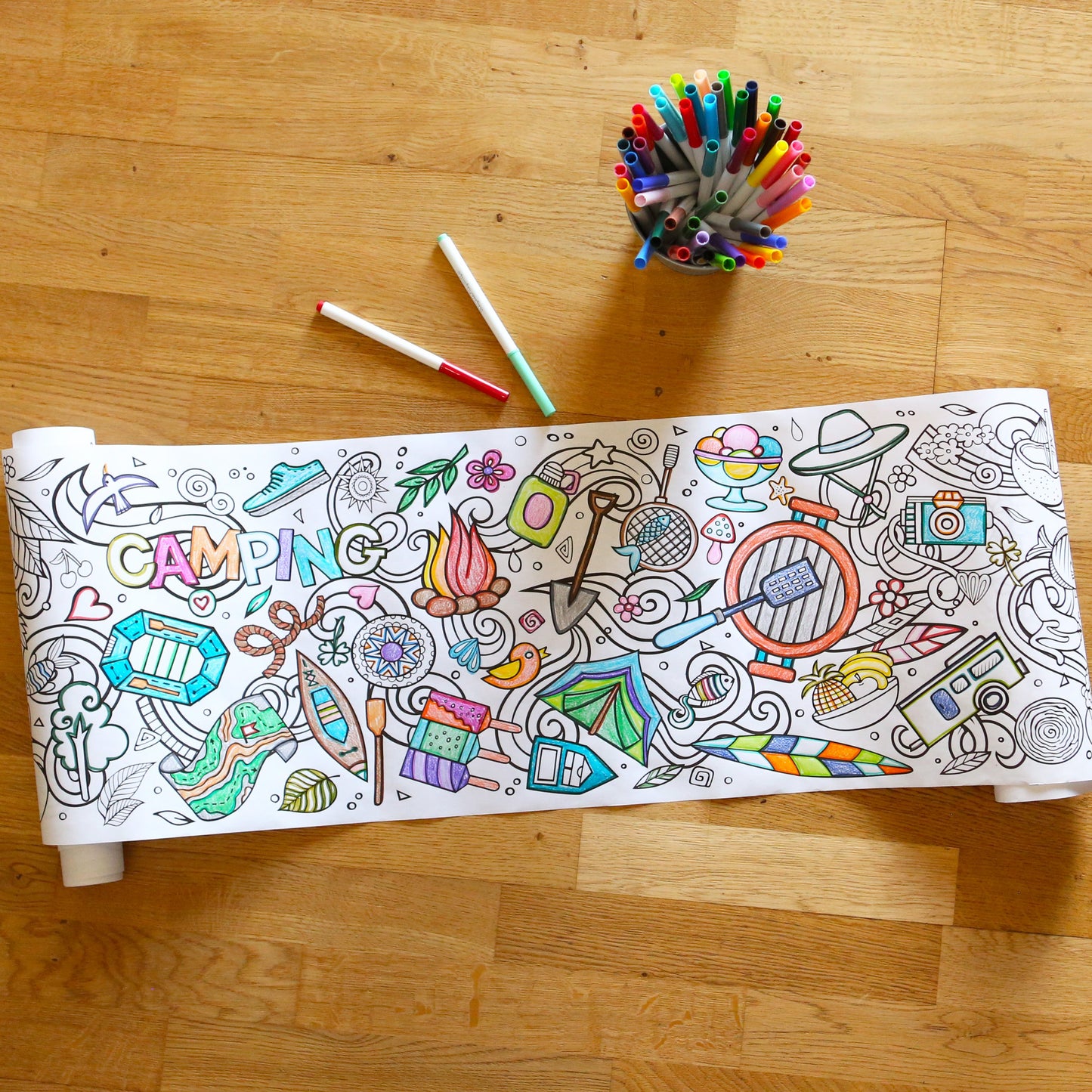 Summer coloring roll on hard wood floor with markers in a bucket.