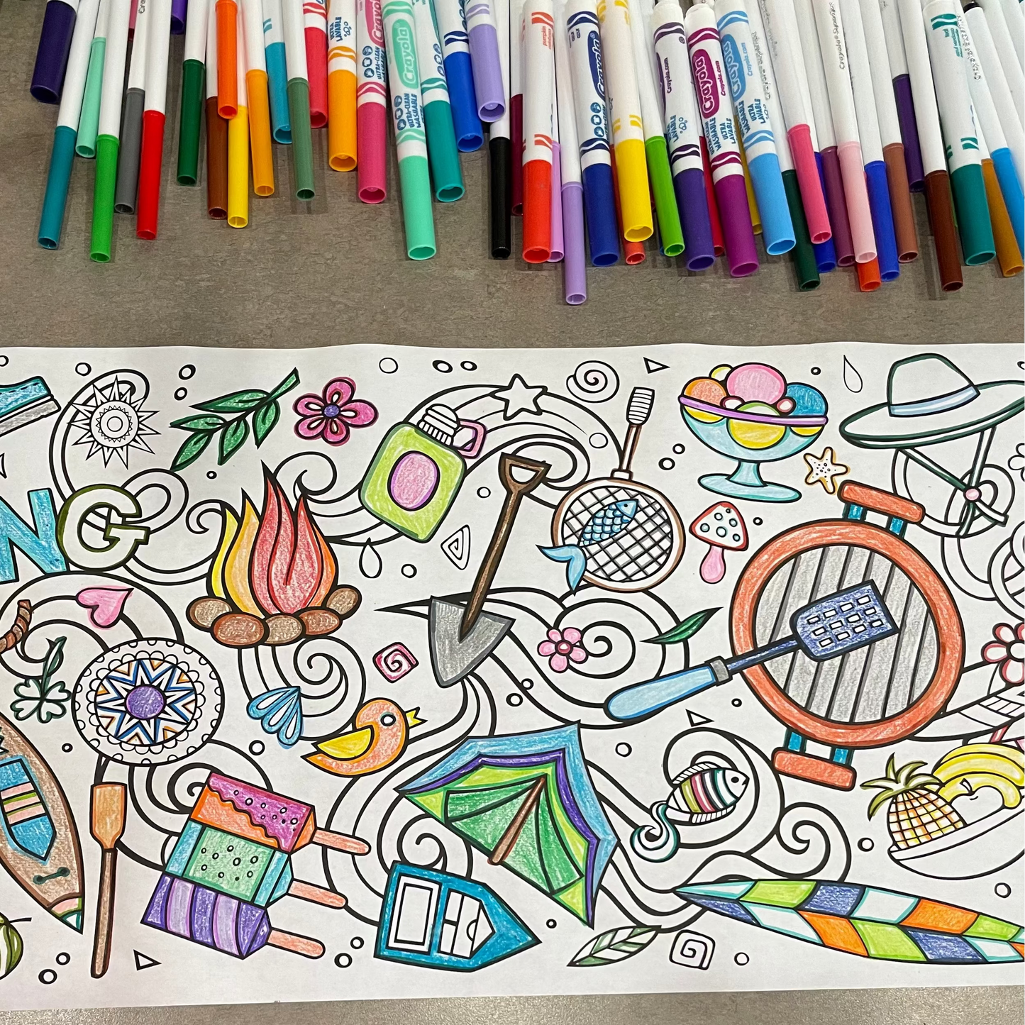 Coloring coloring roll with a row full of bright markers. Coloring roll has been colored with crayons and is filled with camping and summer graphics.
