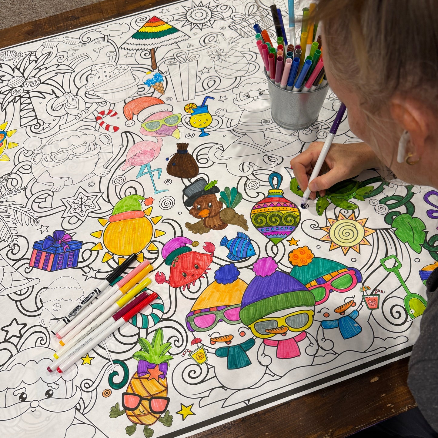 Person coloring a detailed and colorful tropical christmas coloring sheet - adult coloring poster on a wooden table.